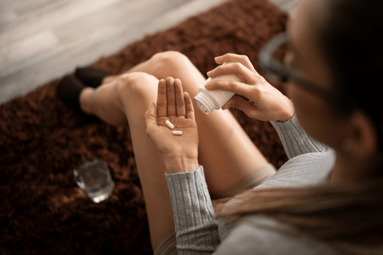 overhead view of a person holding pills in one hand and a glass of water in the other