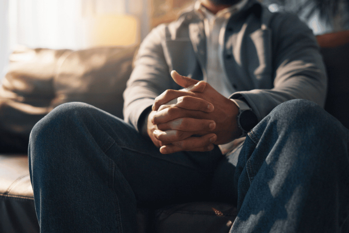 man sitting on the edge of a bed with his hands clasped and head lowered