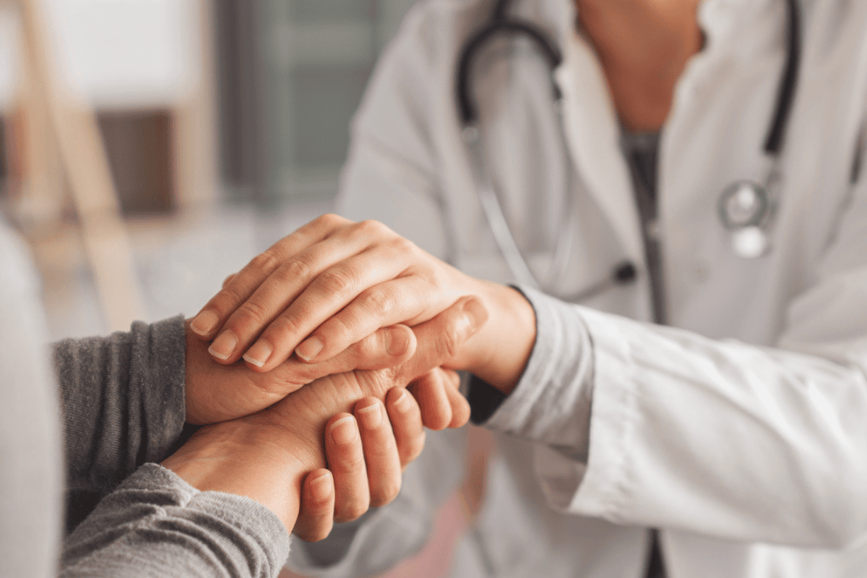 person resting a comforting hand on someone's arm during a medical visit