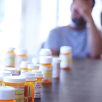 man sitting at a table with his head in his hand behind a row of prescription bottles