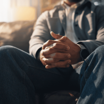 man sitting on the edge of a bed with his hands clasped and head lowered