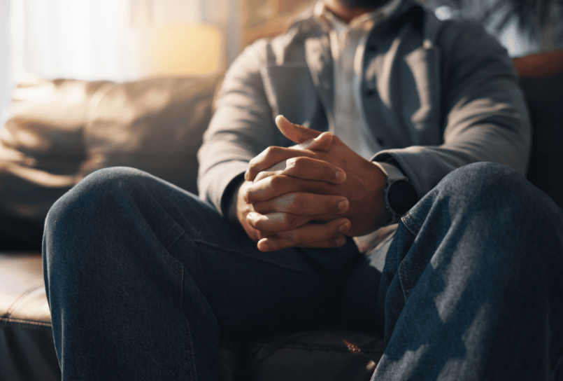 man sitting on the edge of a bed with his hands clasped and head lowered