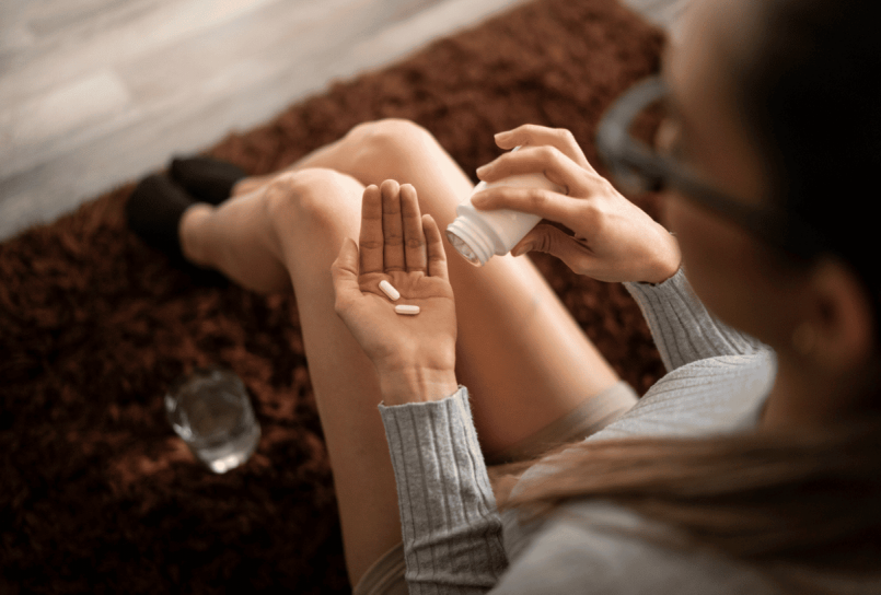 overhead view of a person holding pills in one hand and a glass of water in the other