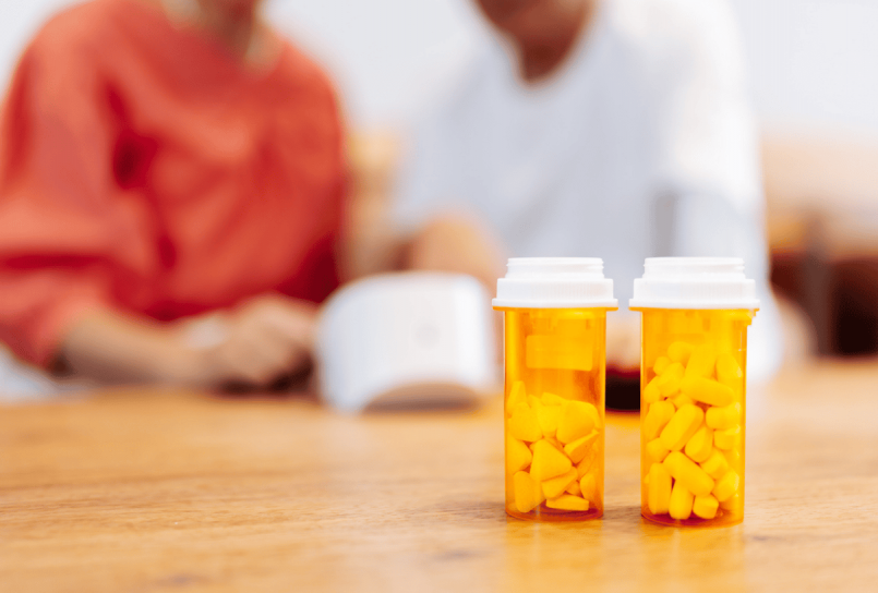 prescription bottles on a table with a provider and patient talking in the background